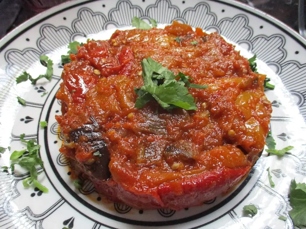 Salade d'aubergines à la tomate et au poivron servie dans une assiette décorée